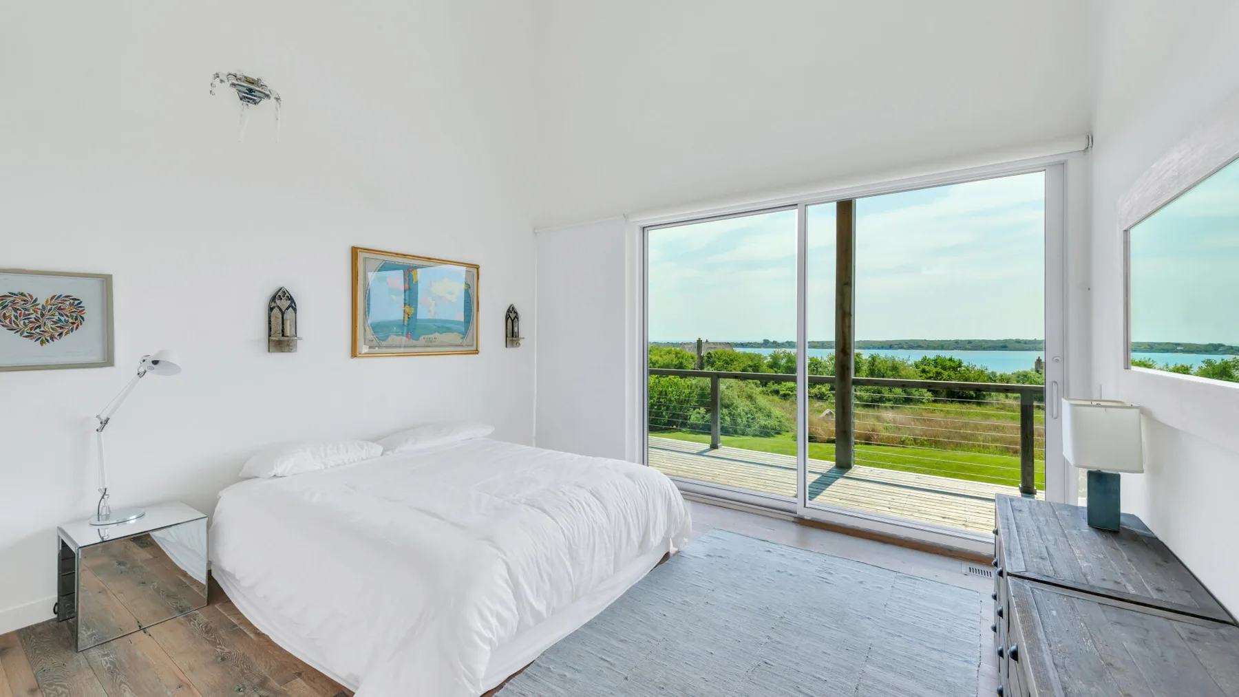 A bright bedroom with a bed beside large glass doors opening onto a balcony.