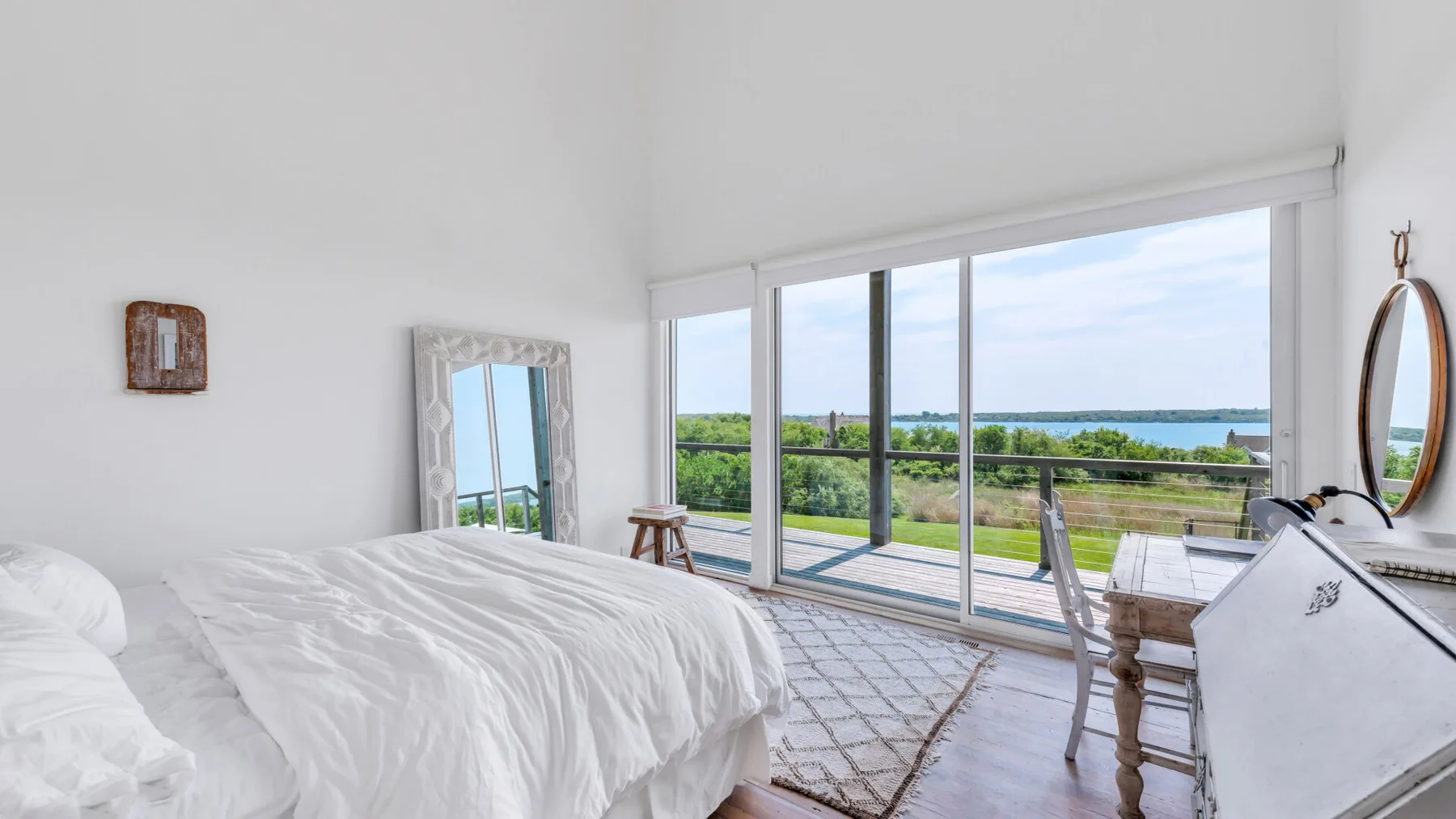 A bright bedroom opens onto a balcony with views of greenery and water.