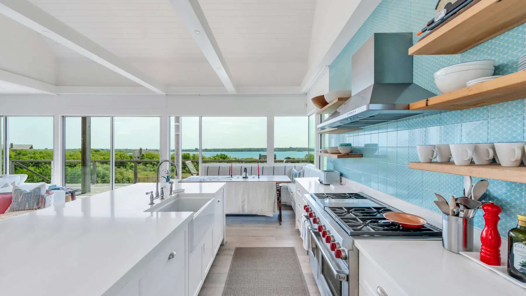 A bright modern kitchen with a long island and large windows overlooking greenery and water.