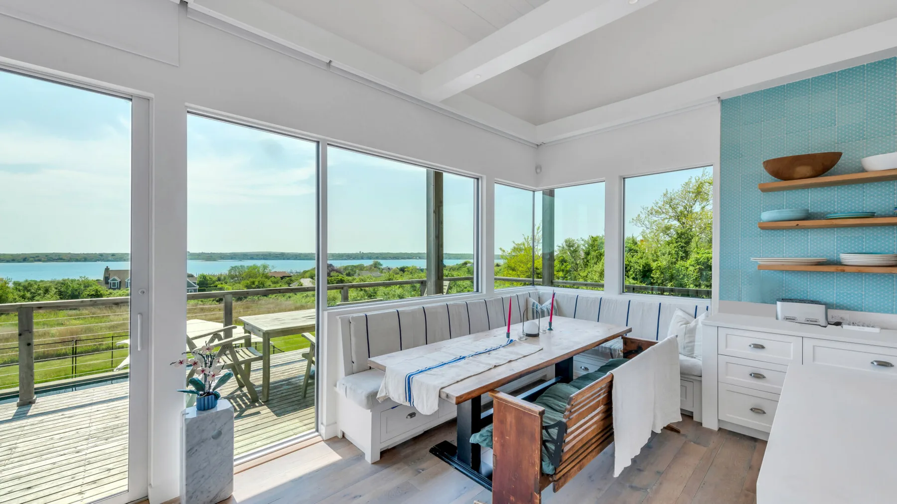 A bright dining area with a built-in bench and large windows overlooking greenery.