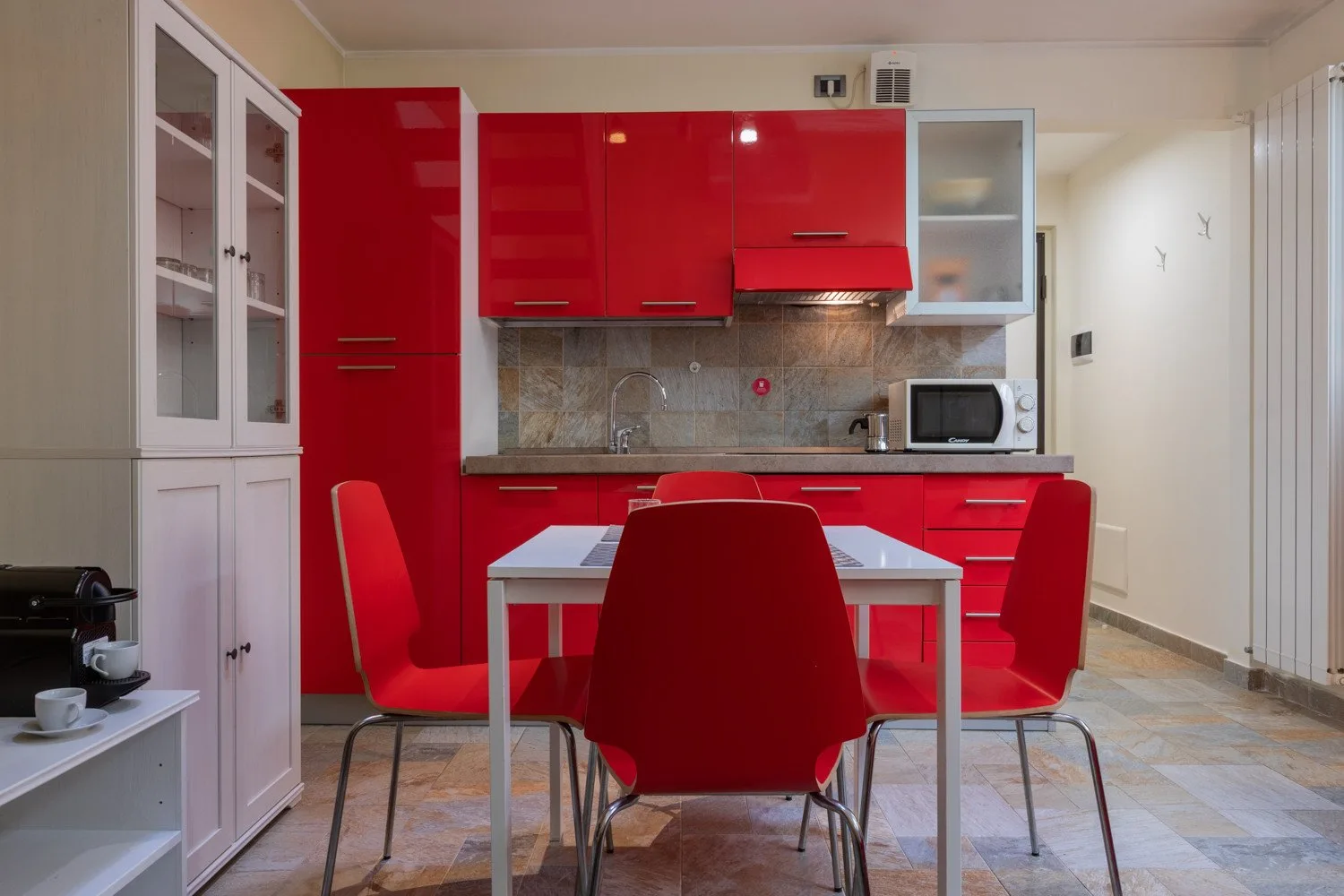 Una mesa de comedor con asientos rojos está frente a una cocina de color rojo intenso.