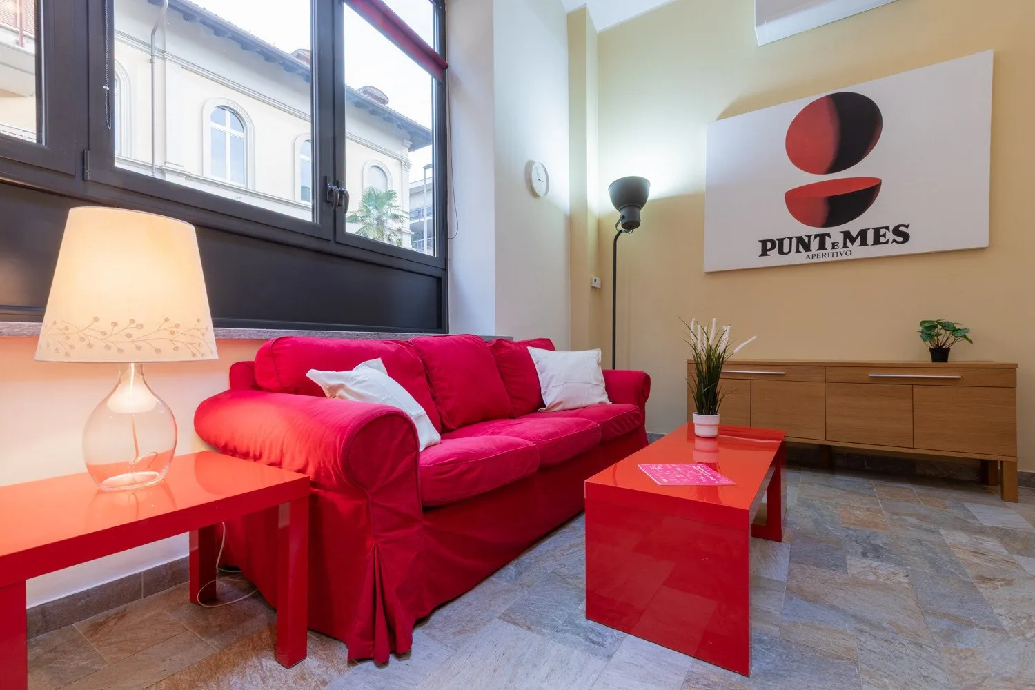 Una sala luminosa con un sofá rojo, una mesa de centro a juego y ventanas grandes.