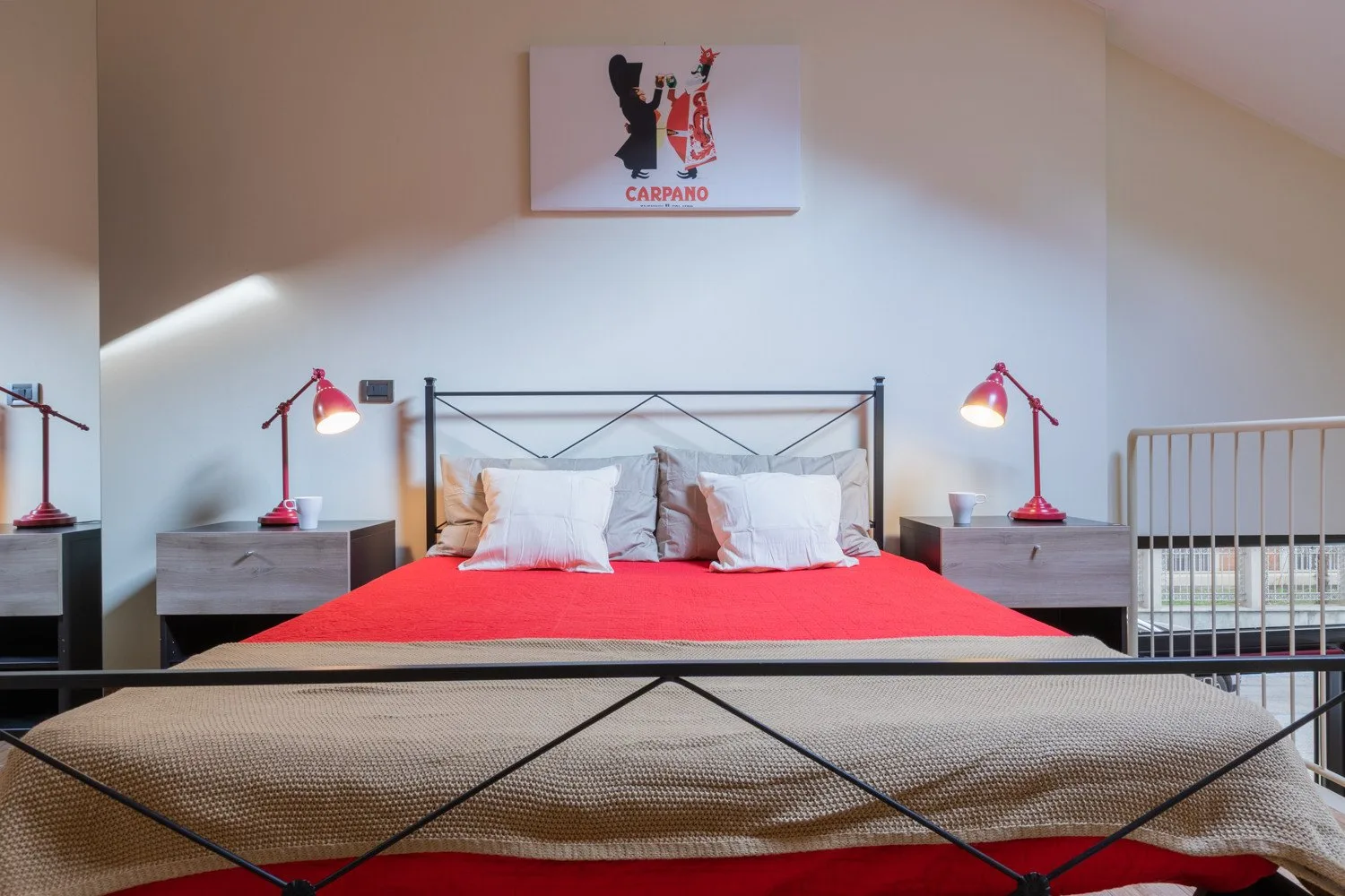 Un dormitorio con una colcha roja, almohadas blancas y lámparas de mesilla a juego.