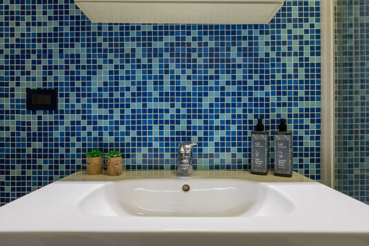 Un lavabo blanco está frente a una pared cubierta de mosaicos azules.