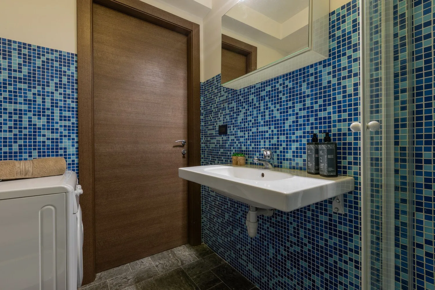 Un baño alicatado con lavabo, espejo y lavadora.