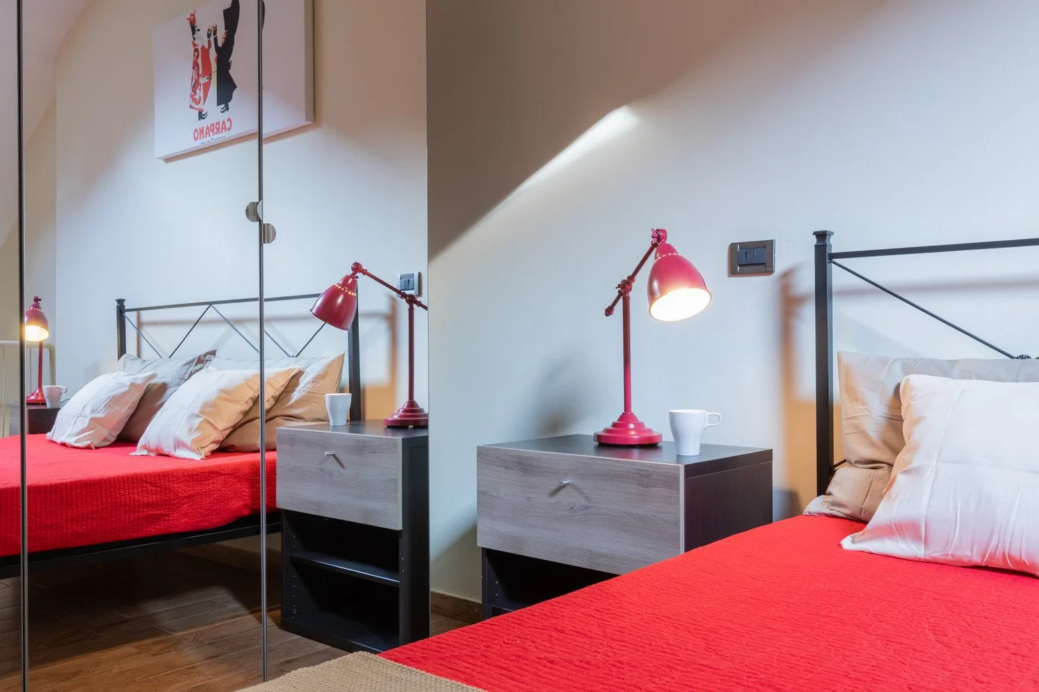 Un dormitorio con ropa de cama roja y lámparas junto a puertas de armario con espejo.