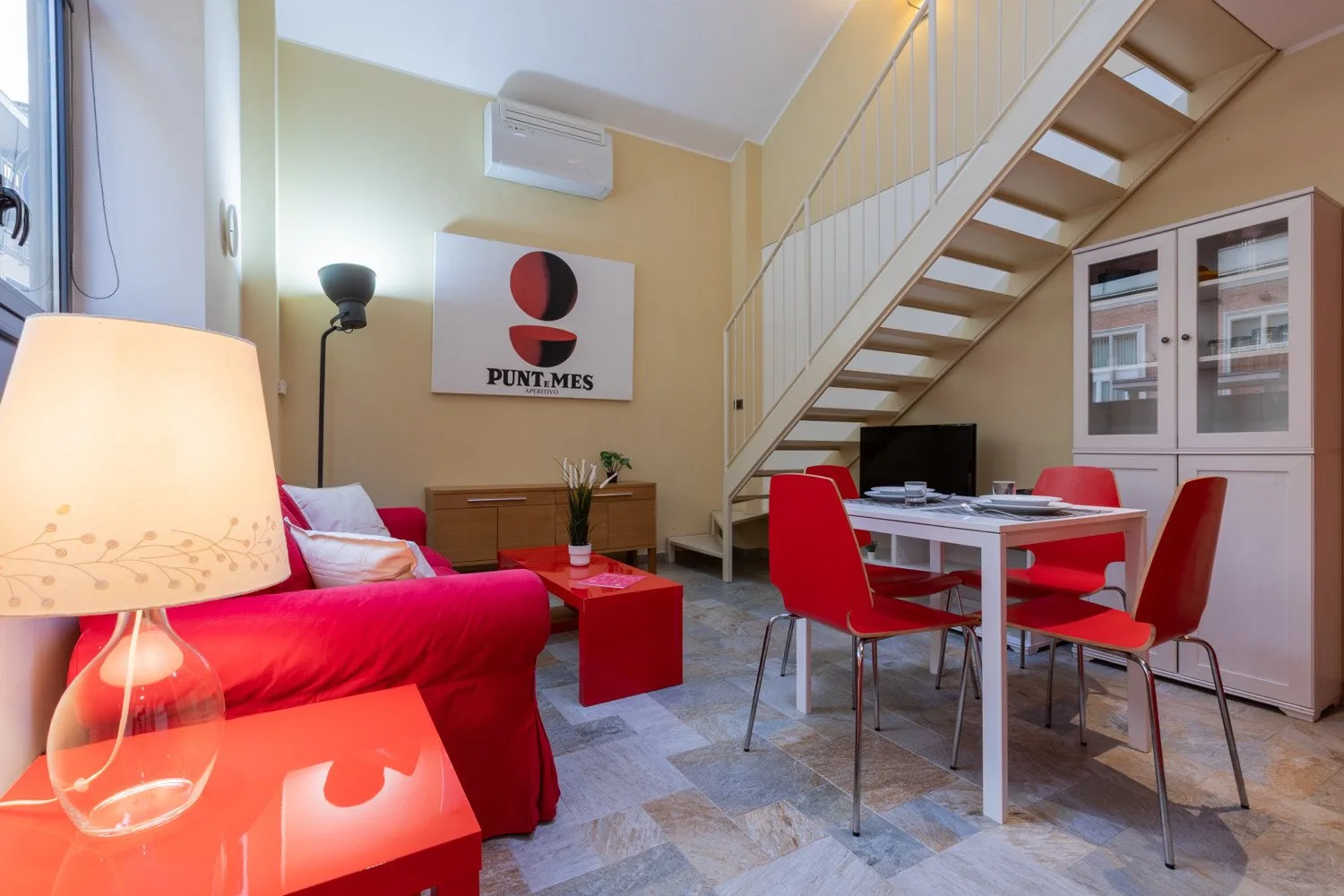 Una sala de estar y comedor con asientos rojos, una mesa y una escalera.