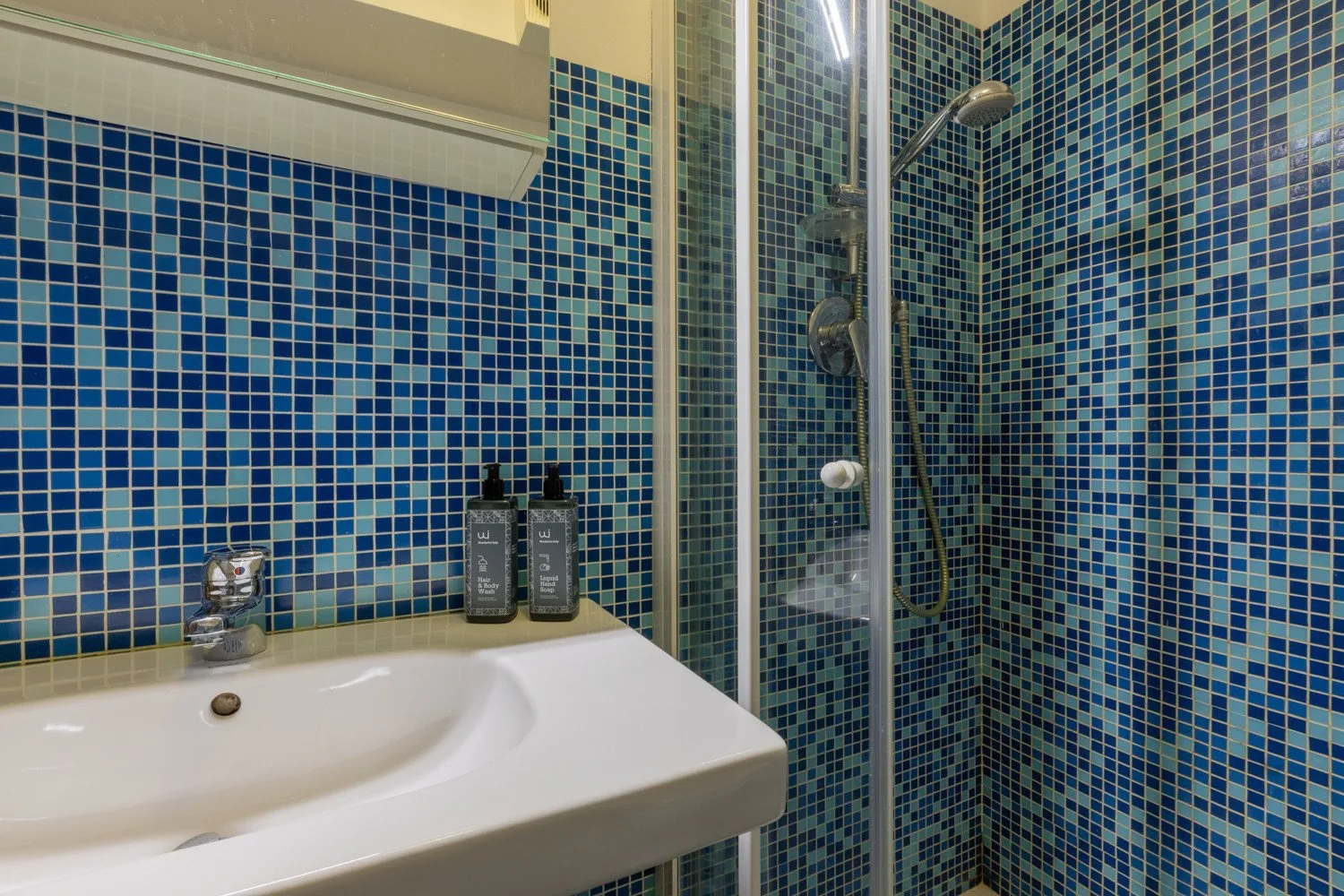 Un baño con un lavabo blanco junto a una ducha revestida de azulejos.