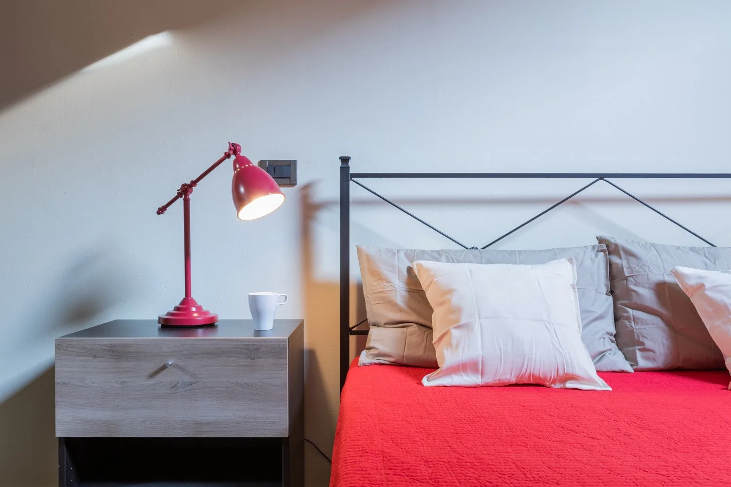 Un dormitorio con una cama cubierta de rojo, almohadas y una lámpara de noche.
