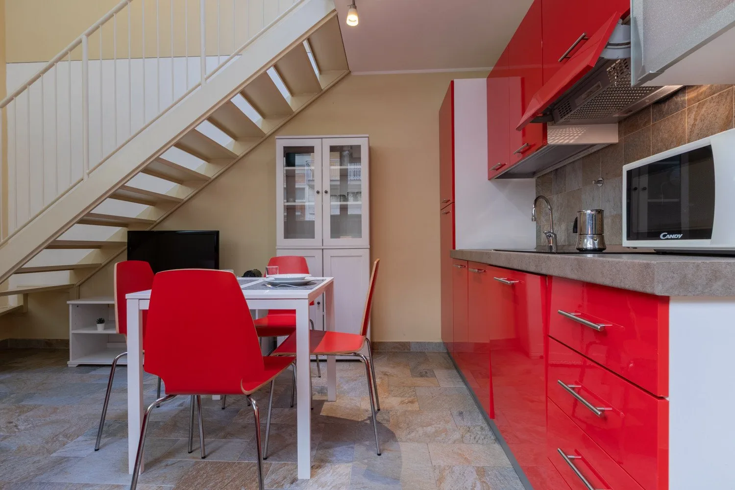 Comedor y cocina con gabinetes rojos y una mesa bajo una escalera.