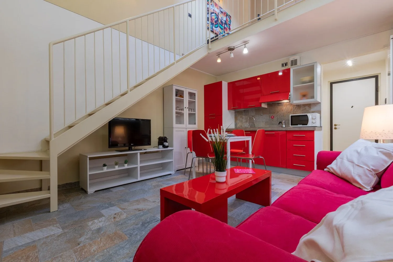 Una sala de estar con asientos rojos y una cocina compacta bajo una escalera.