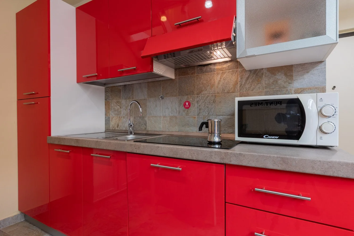 Una cocina con gabinetes rojos, un fregadero y un microondas.