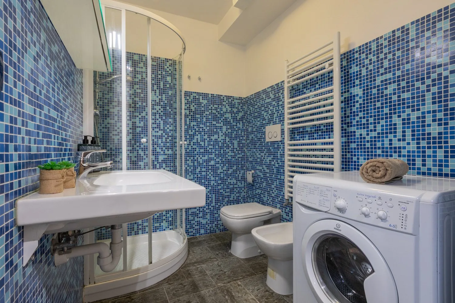 Un baño con azulejos, lavabo, ducha, inodoro y lavadora.