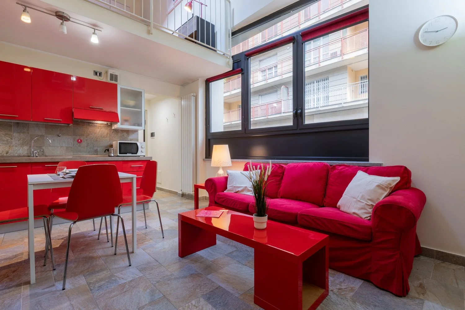 A bright living room with red seating, a dining table, and an open kitchen.