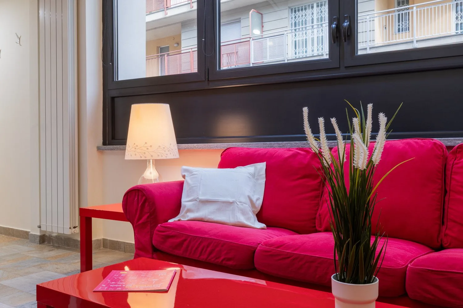 Una sala de estar con un sofá rojo, una lámpara y una planta en maceta.