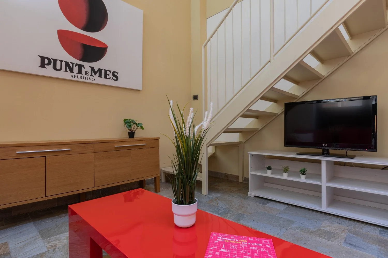 Una sala de estar con una mesa de centro roja, un televisor y escaleras.