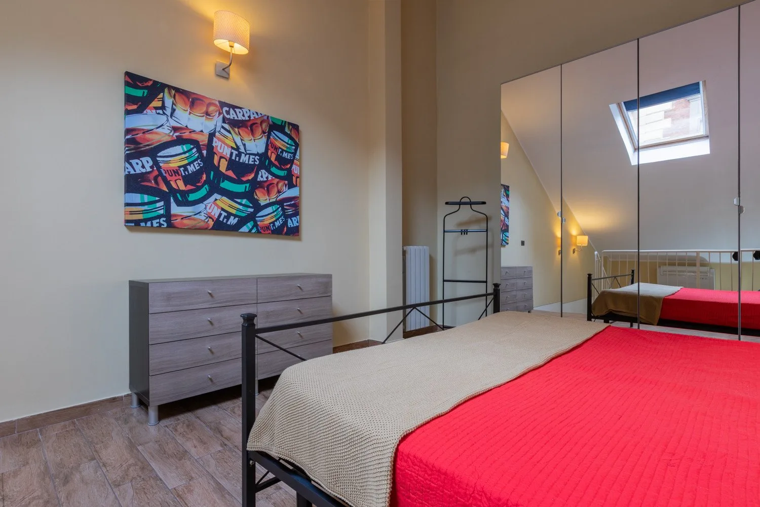Un dormitorio con una colcha roja, una cómoda y puertas de armario con espejos.