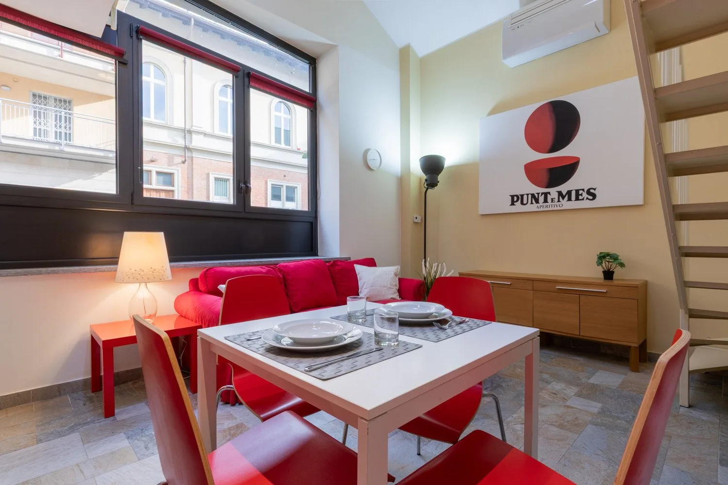 Un comedor con una mesa y asientos rojos junto a grandes ventanas.