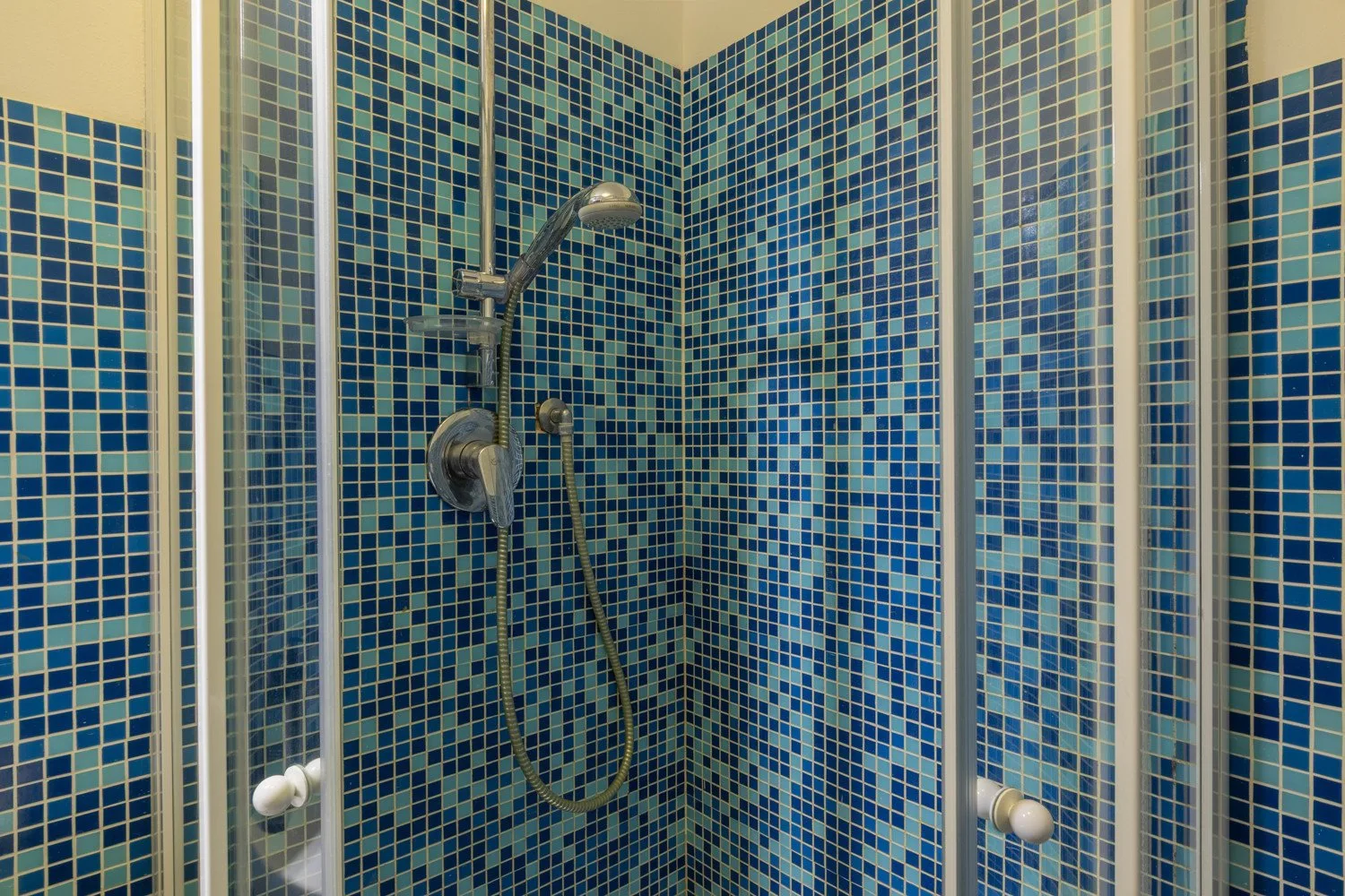Una ducha con paredes de mosaico azul y un cabezal de ducha.