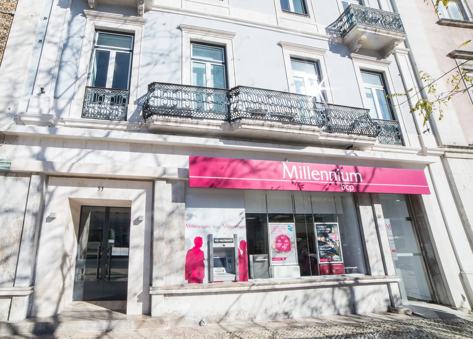 La fachada de un edificio blanco tiene balcones ornamentados sobre un local con un letrero rosa.