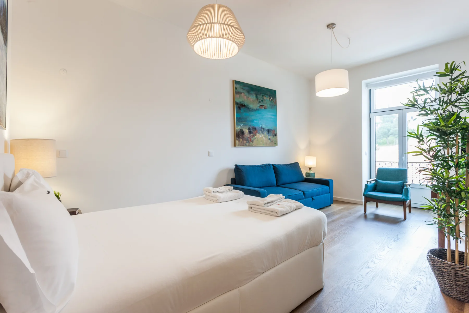 Un dormitorio tipo estudio luminoso con cama, asientos azules y una ventana grande.