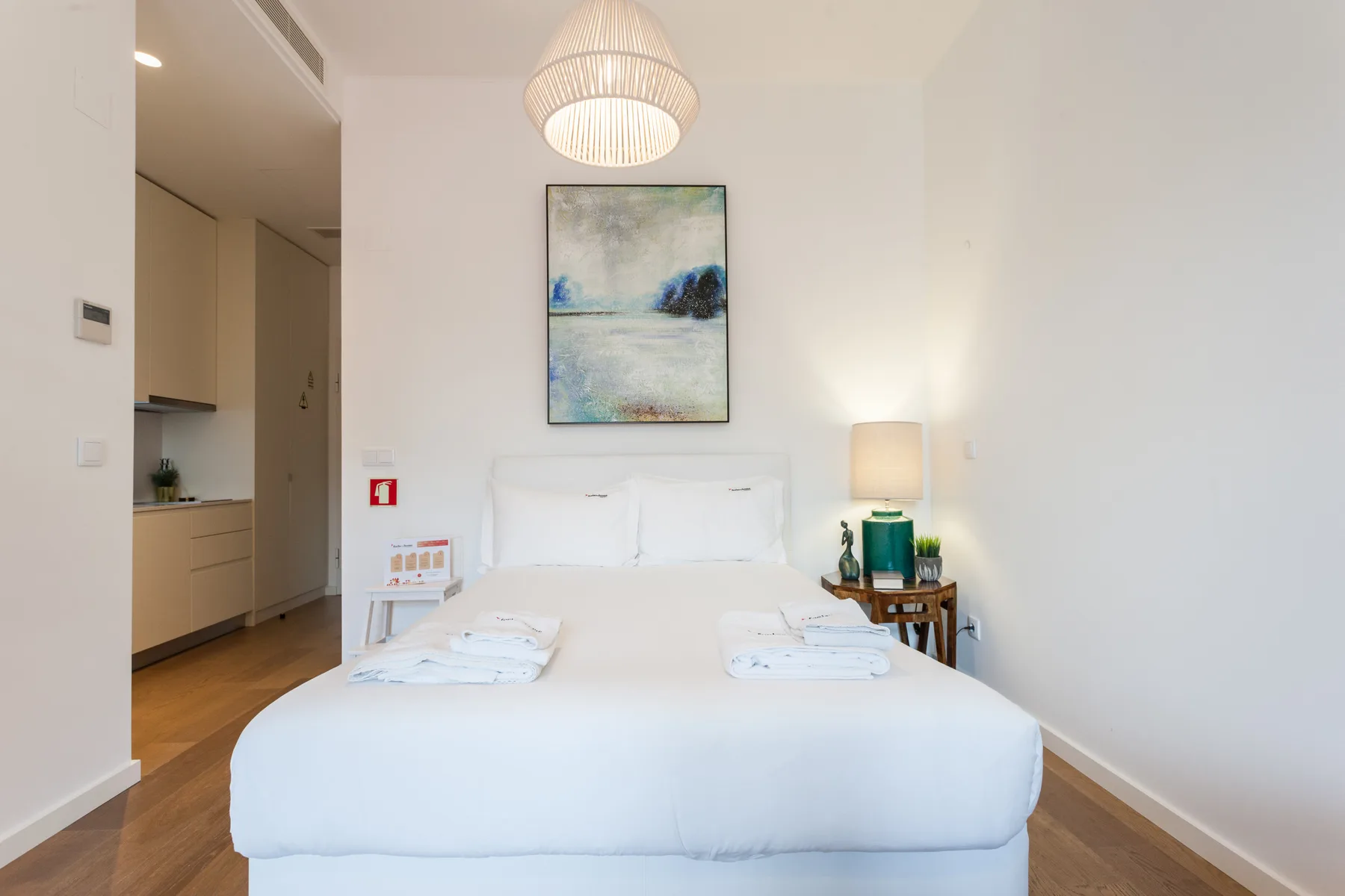 Un dormitorio luminoso con una cama bien tendida y una obra de arte sobre el cabecero.