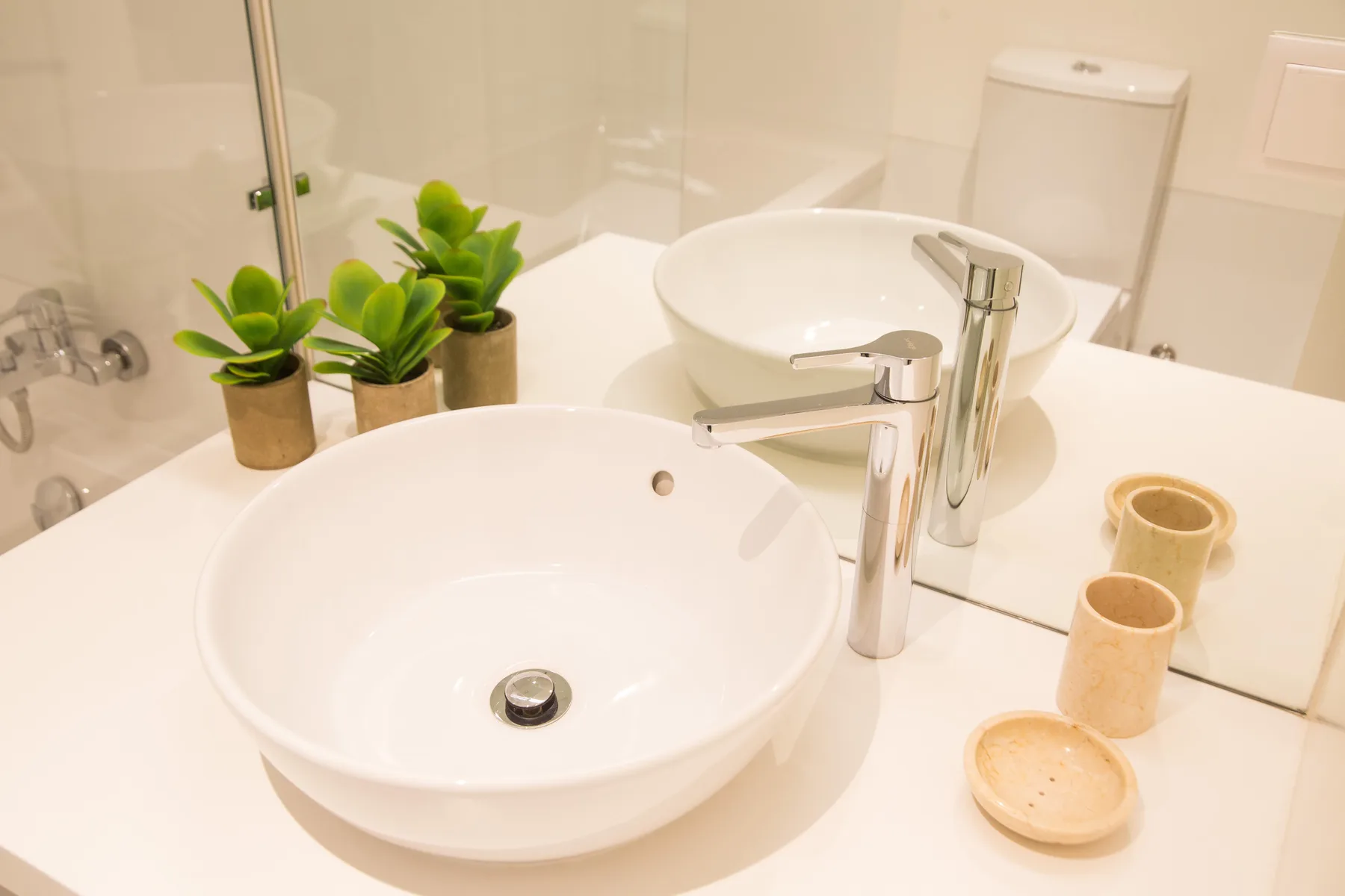 Un lavabo de baño con una pila blanca, grifo cromado y pequeñas plantas en macetas.