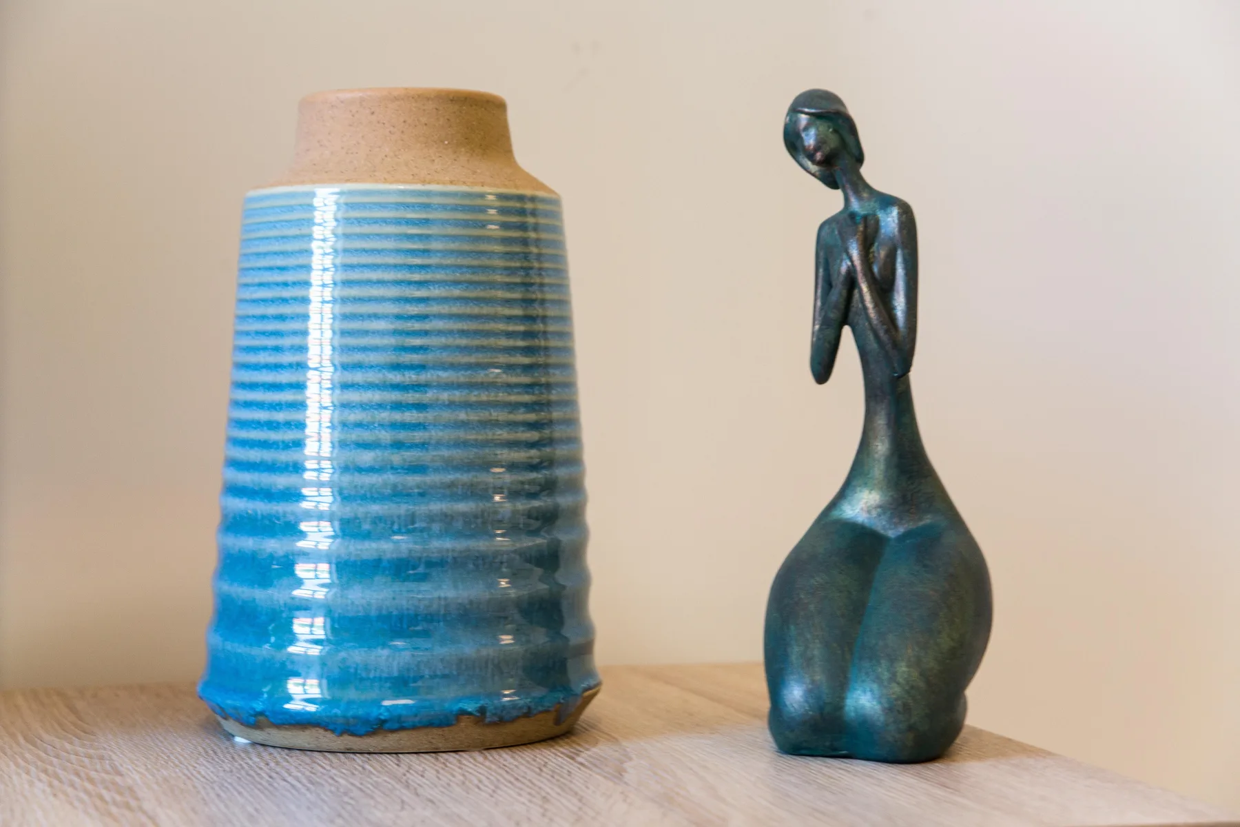 Un jarrón azul de cerámica y una pequeña escultura están sobre una superficie de madera.