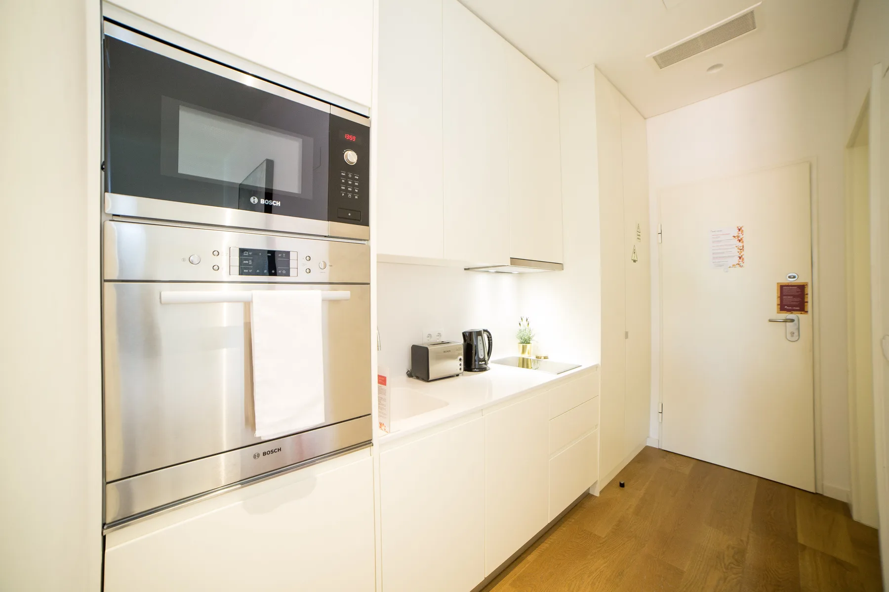Una cocina blanca y luminosa con electrodomésticos integrados y suelo de madera.