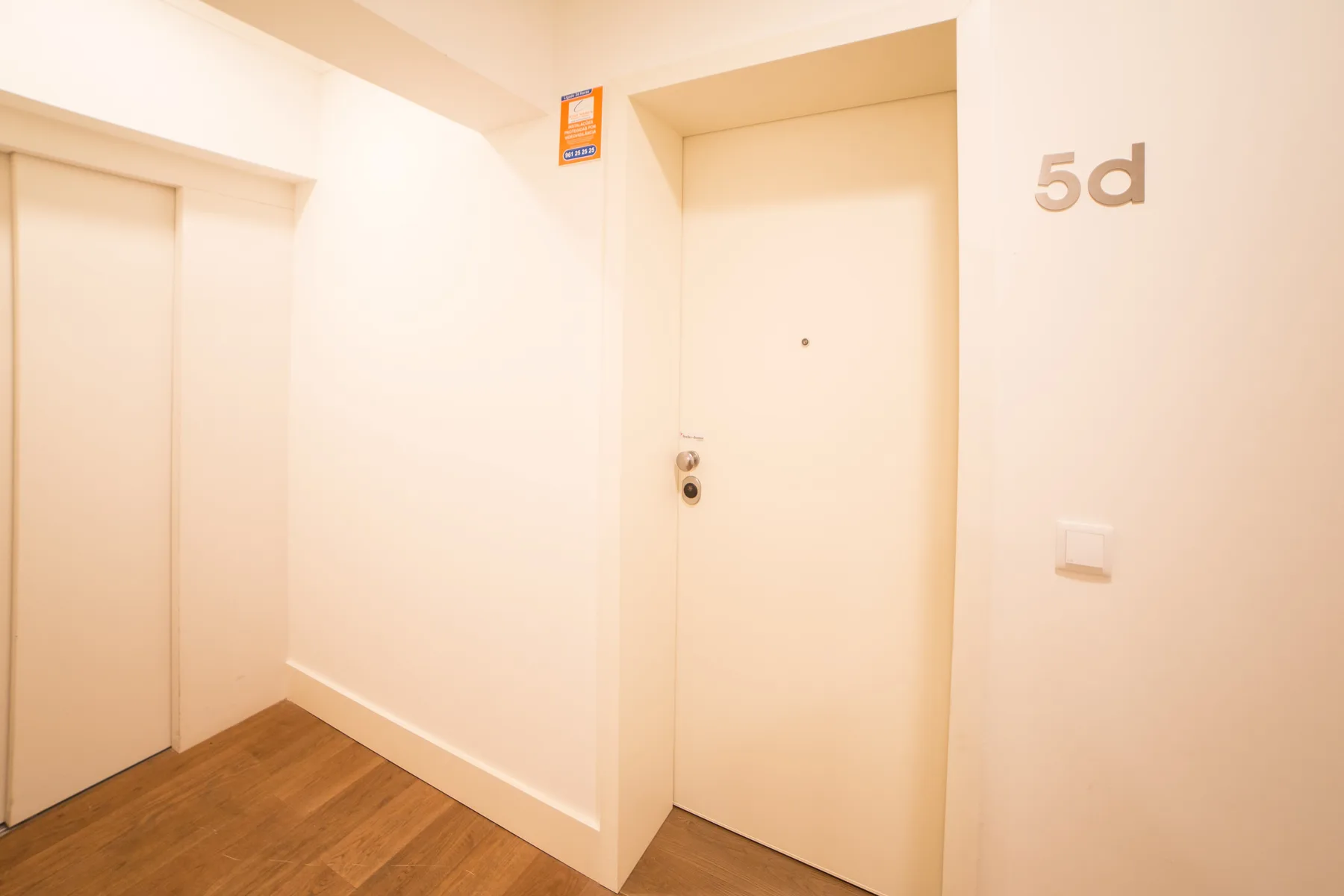 Un pasillo de apartamento con una puerta de entrada cerrada y suelo de madera.
