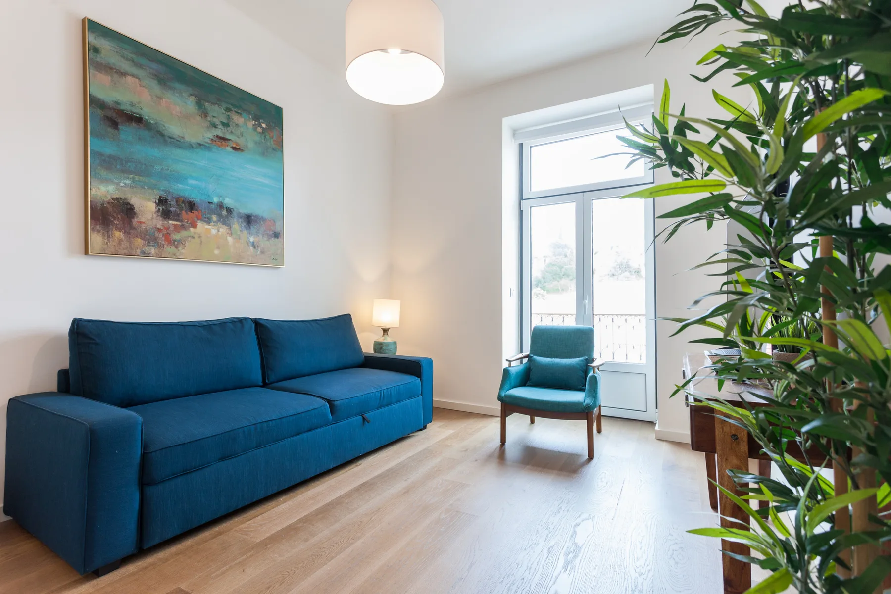 Una sala luminosa con asientos azules, una ventana amplia y una planta frondosa.