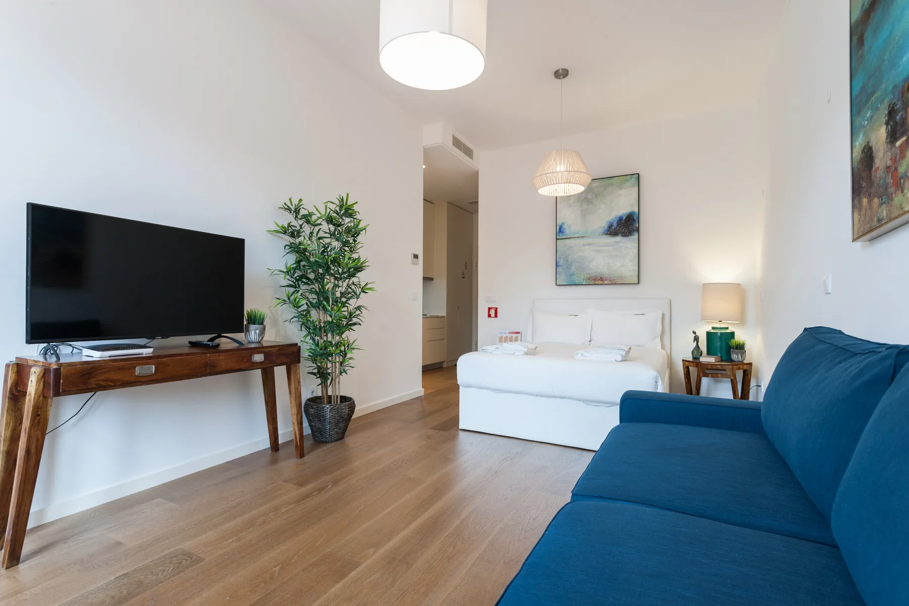 Una luminosa zona de estar tipo estudio con sofá azul, televisor y cama.