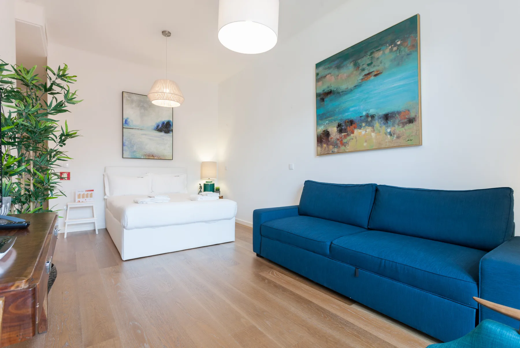 Una luminosa zona de estar tipo estudio con un sofá azul y una cama blanca.