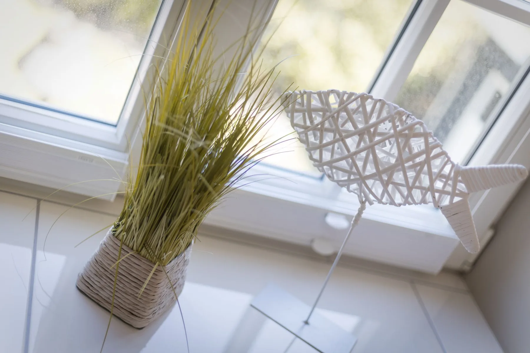 Un rincón luminoso junto a la ventana con una maceta tejida y un pájaro decorativo.