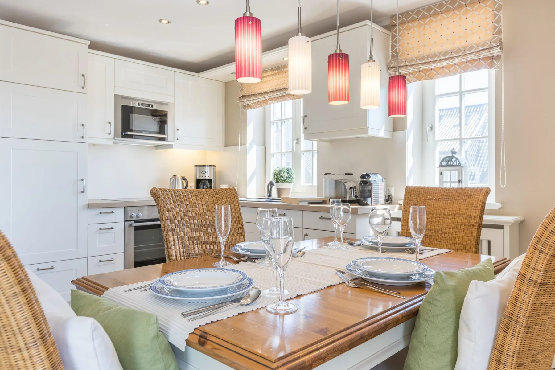 Una luminosa zona de cocina y comedor con la mesa puesta y lámparas colgantes.