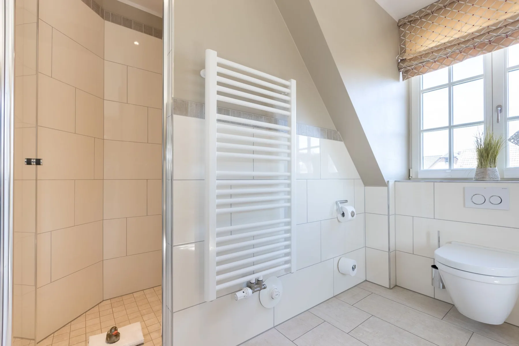 Un baño luminoso con ducha de azulejos, inodoro suspendido y ventana.