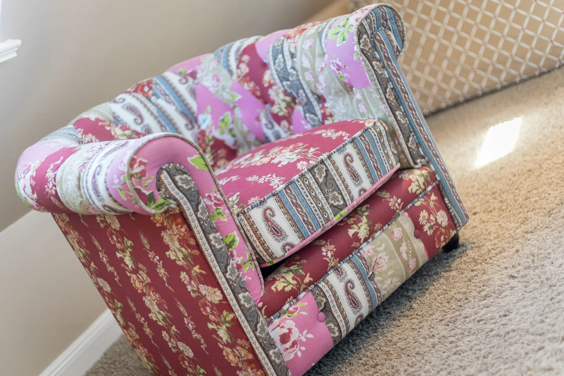 Un sillón tapizado de colores está sobre una alfombra junto a una pared estampada.