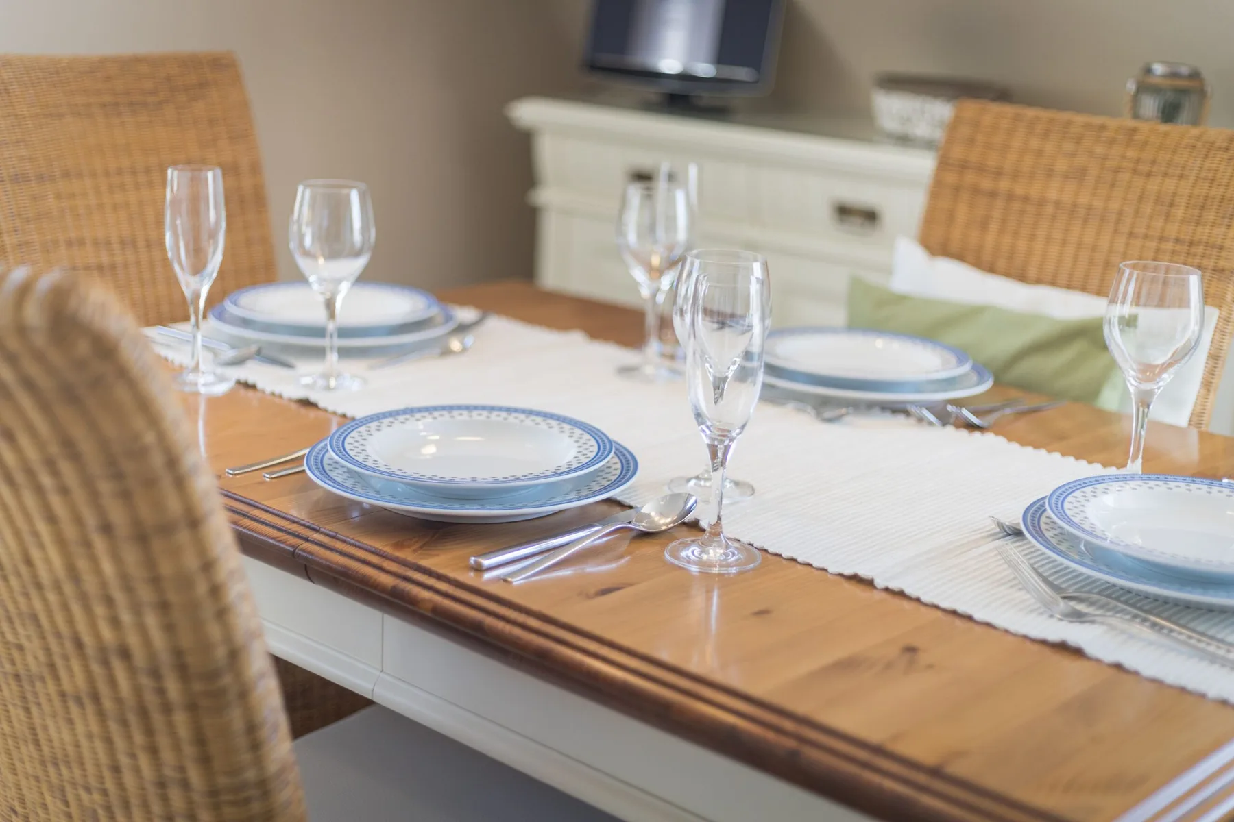 Una mesa de comedor está puesta con platos, cristalería y asientos de mimbre.