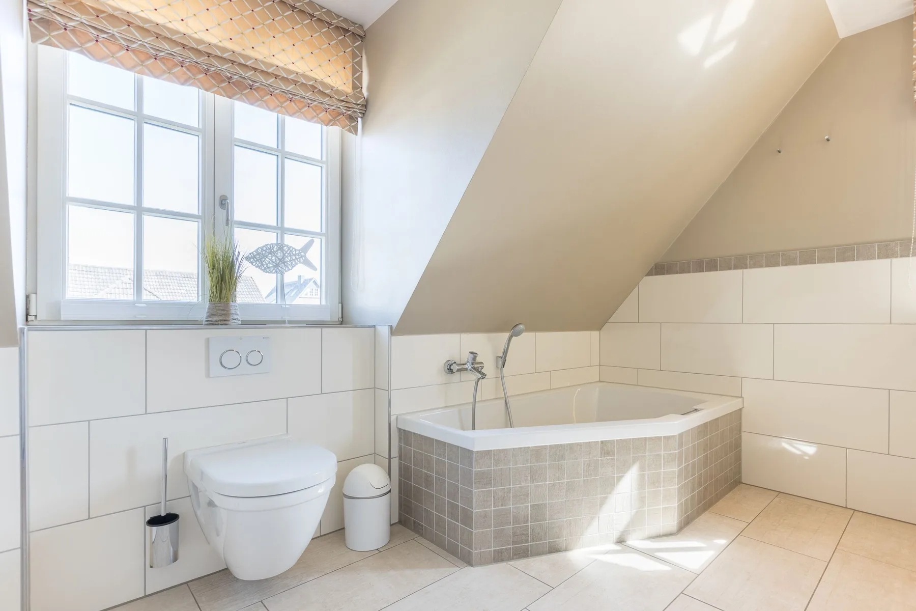 Un baño luminoso con una bañera bajo un techo inclinado y una ventana.