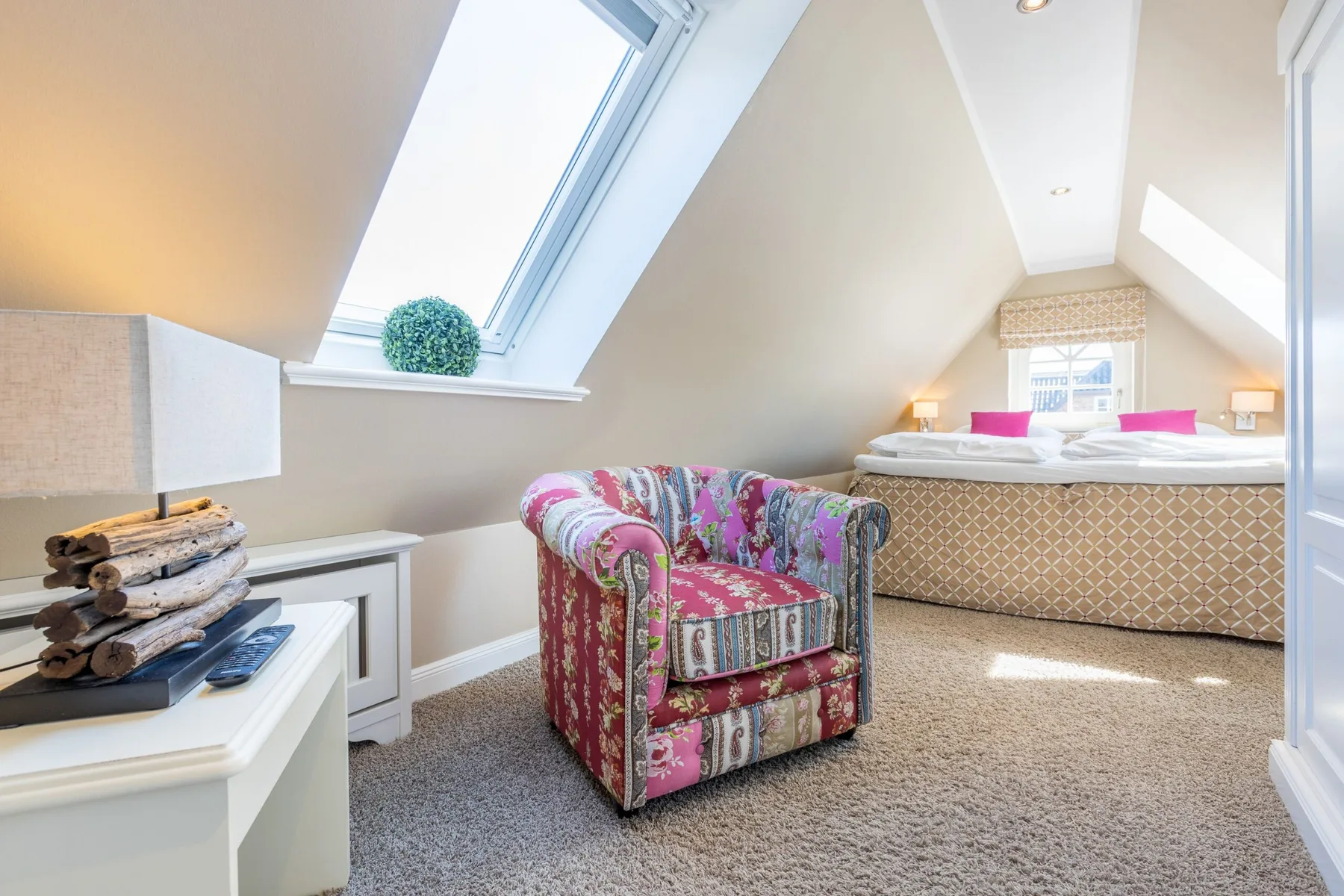 Un dormitorio abuhardillado luminoso con un sillón estampado junto a la cama.