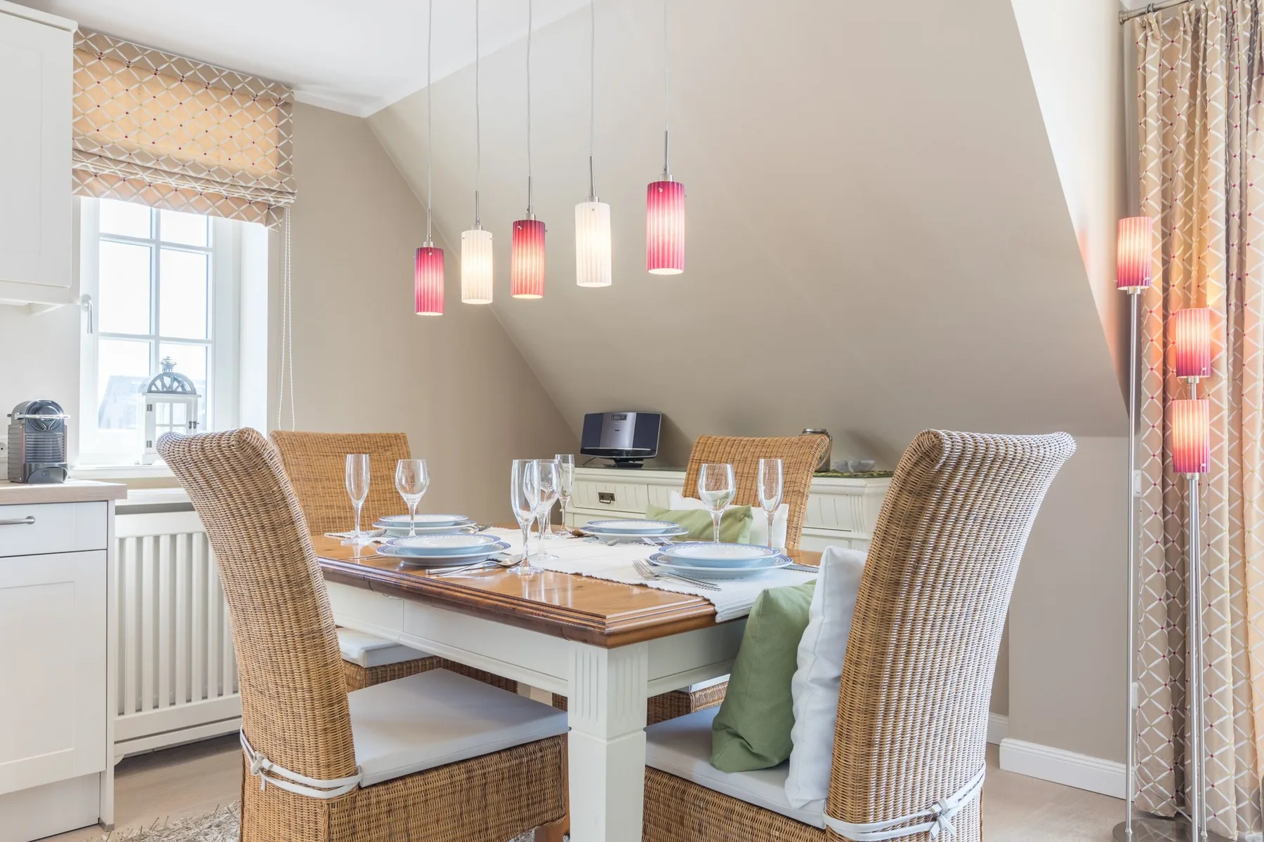Un comedor con la mesa puesta y asientos tejidos bajo lámparas colgantes.