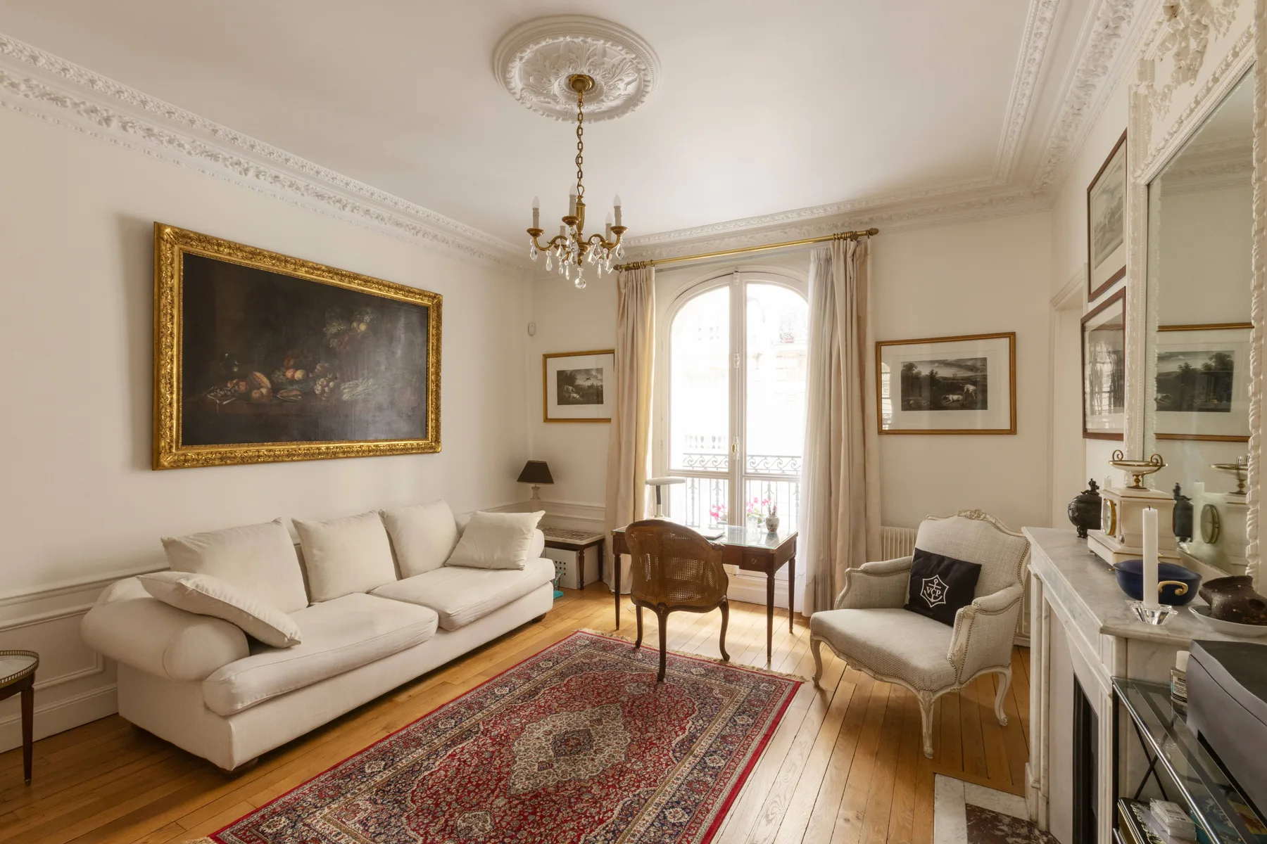 A formal living room with seating, framed paintings, and a large window.