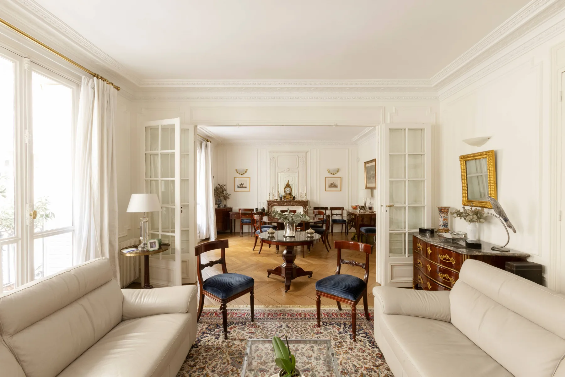 Una luminosa sala de estar con asientos, ventanas altas y un comedor contiguo.