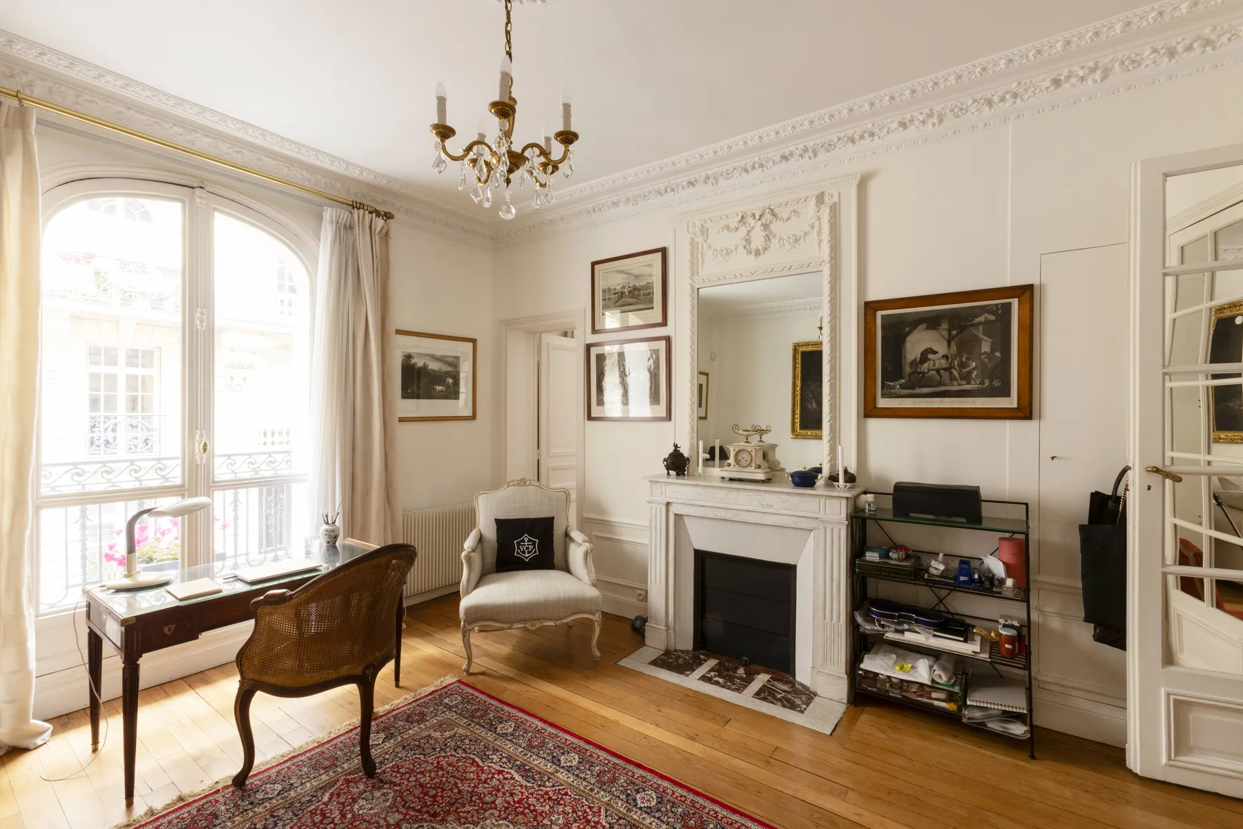 A bright sitting room with tall windows, a fireplace, and framed artwork.
