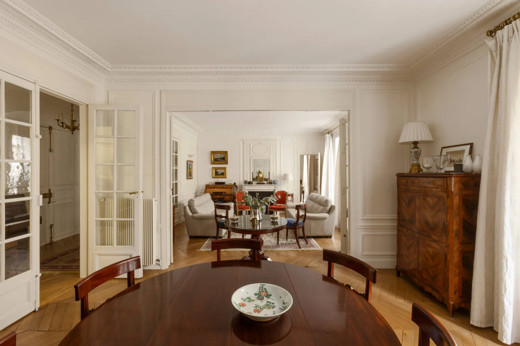 A formal dining room opens onto a sitting area, with a table in the foreground.