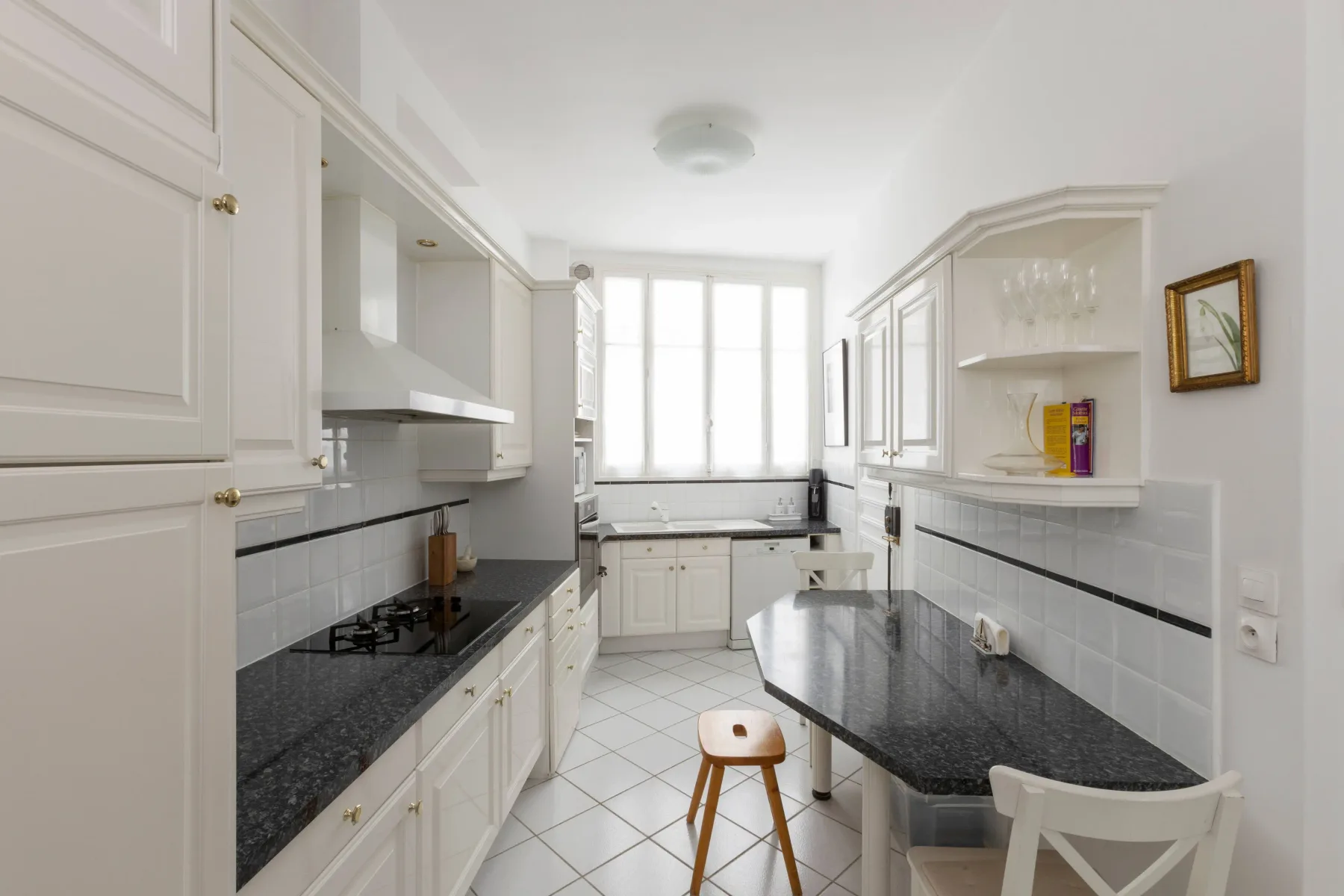 A bright galley kitchen with black countertops and a window at the far end.