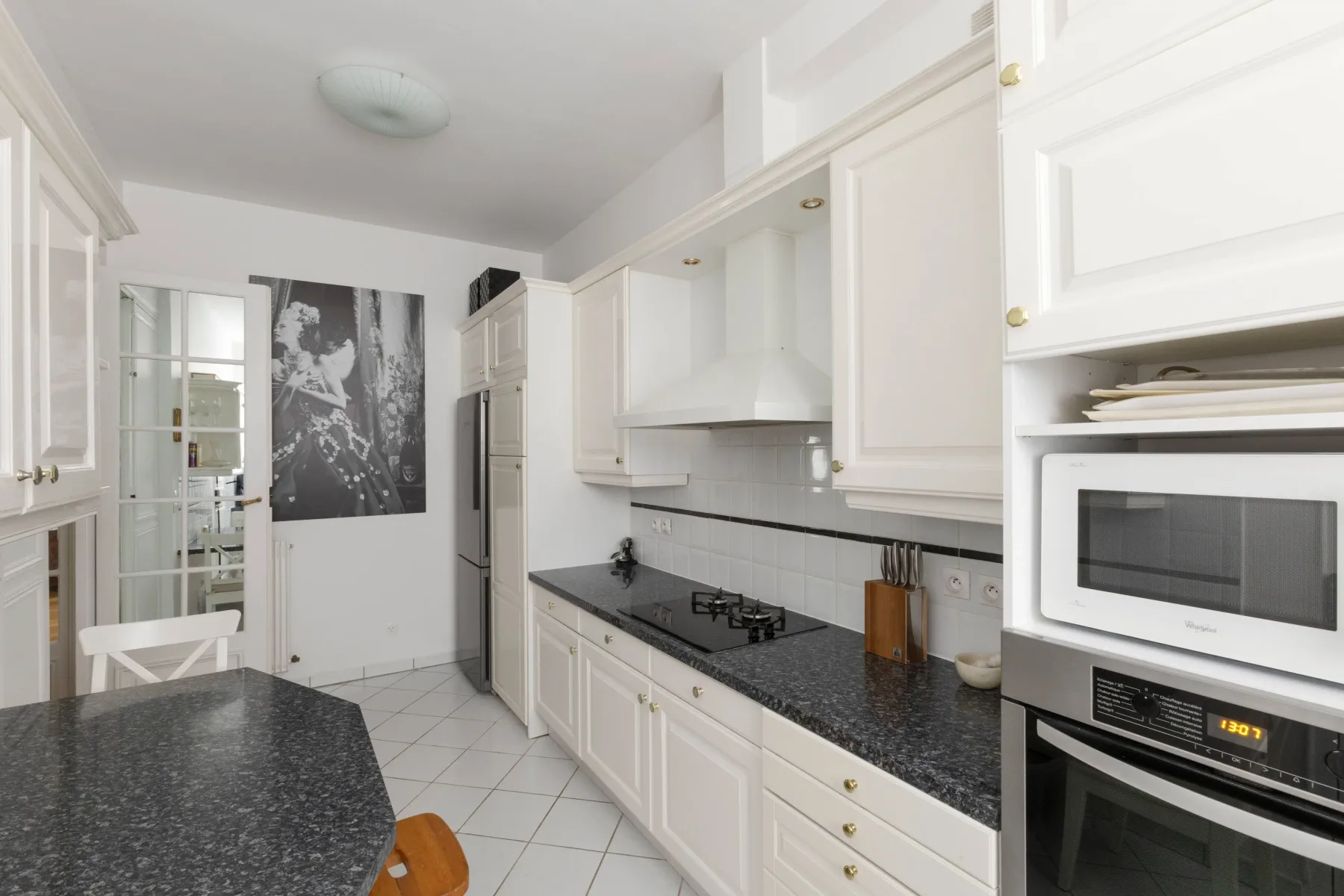 A bright white kitchen with dark countertops and built-in appliances.