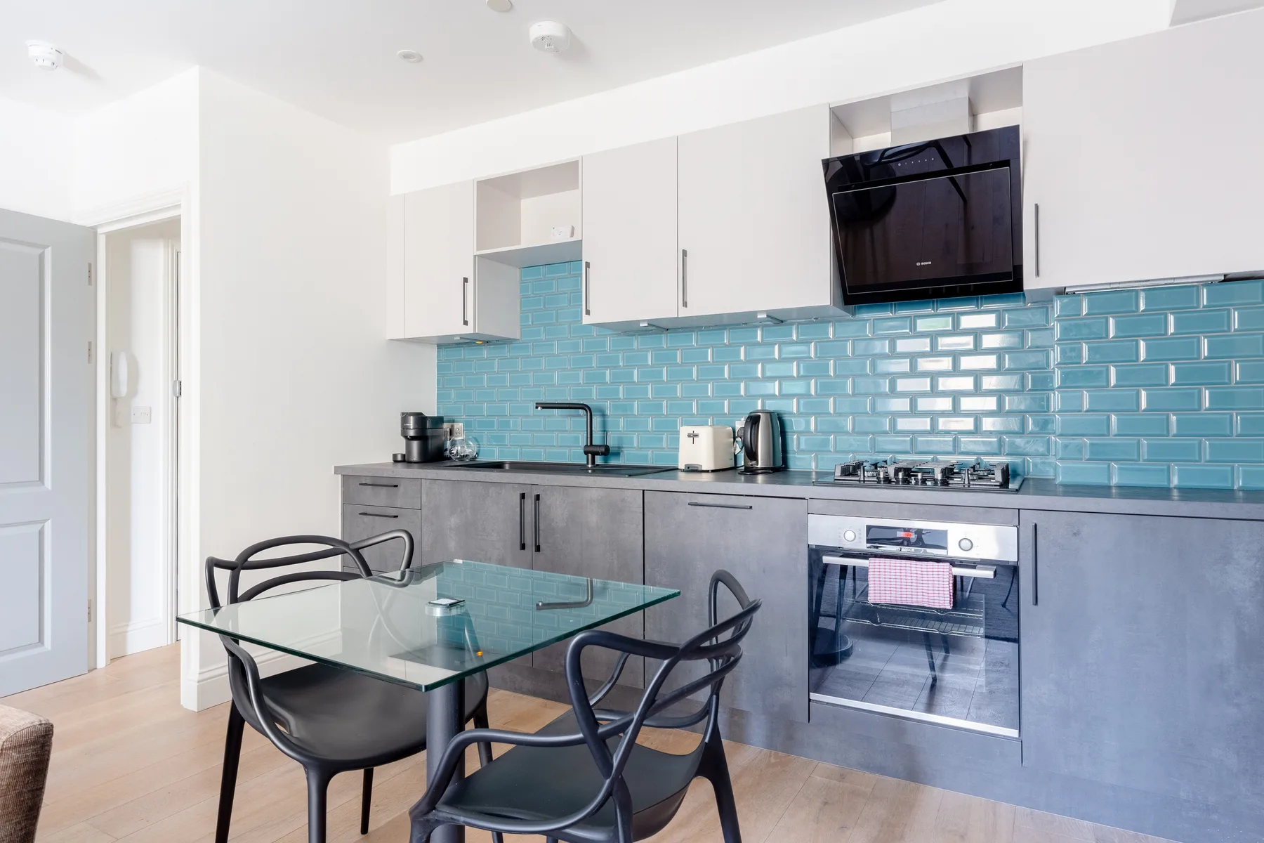 A bright kitchen with a dining table and blue tile backsplash.
