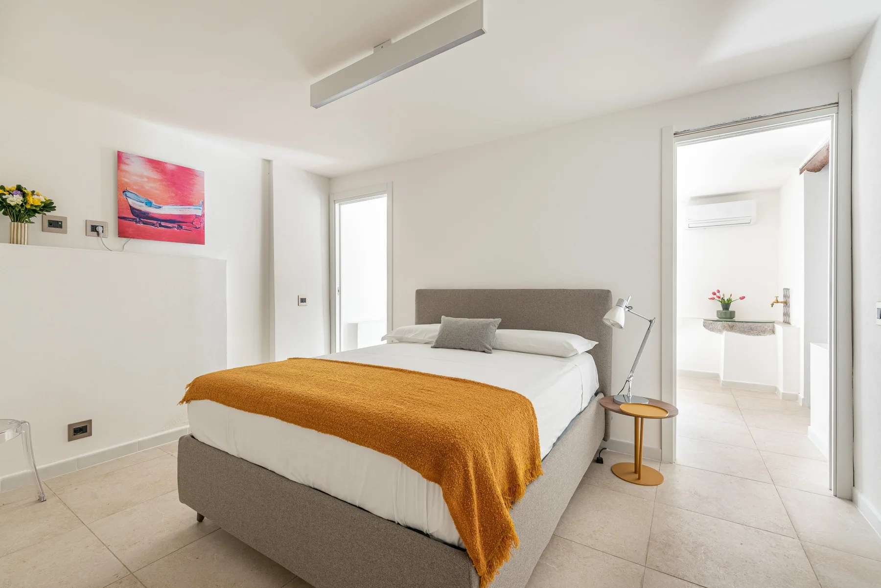A bright bedroom with a bed, colorful wall art, and an open doorway.