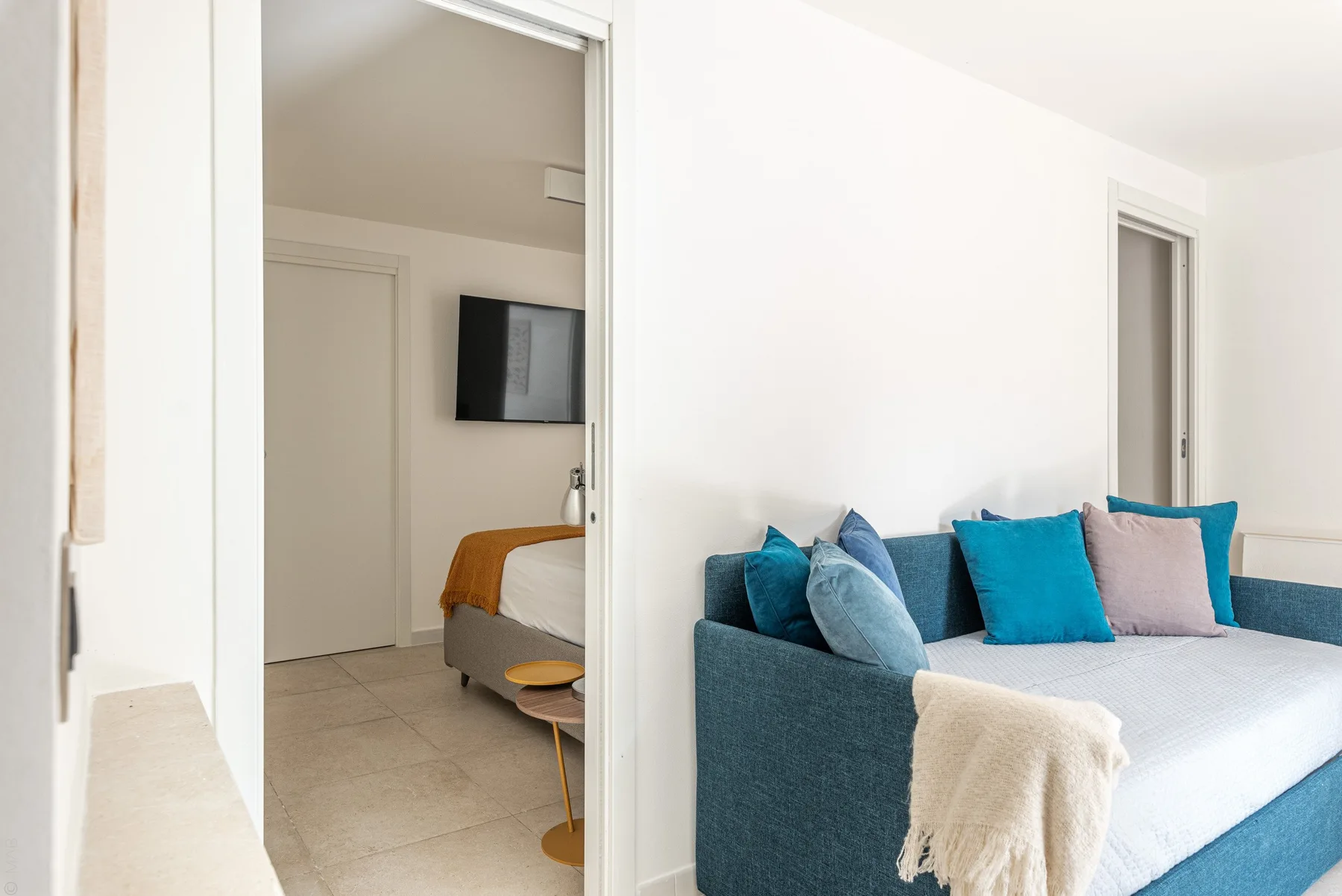 Un dormitorio luminoso con una cama y una zona de asientos turquesa junto a la puerta.